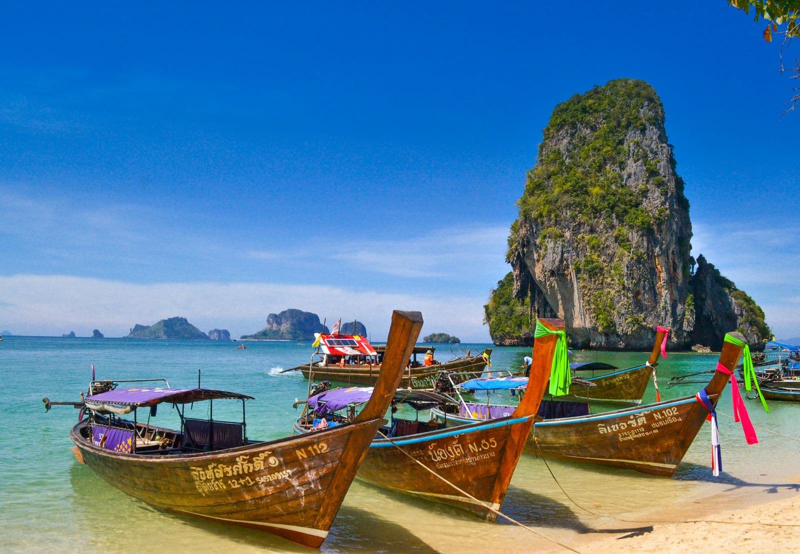 Longtail-Boote am Strand vor einem Kalksteinfelsen bei Krabi, Thailand