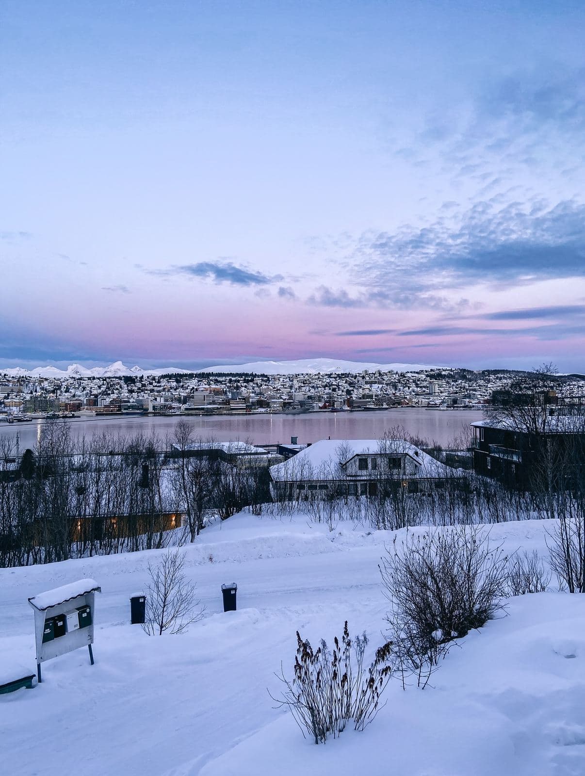 Blick über den verschneiten Sund auf Tromsø in der Abenddämmerung